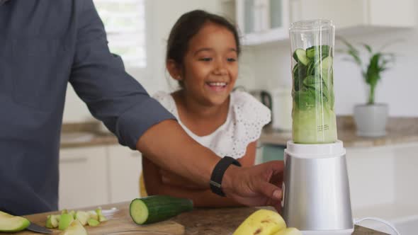 Hispanic father with smiling daughter teaching making smoothie in blender