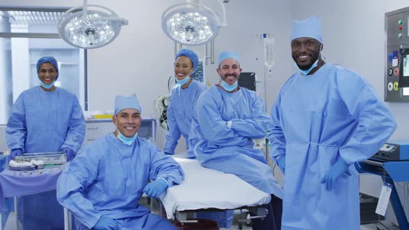 Diverse male and female doctors wearing face masks standing in operating theatre smiling to camera