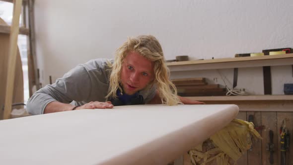 Caucasian male surfboard maker making a surfboard and preparing to polishing