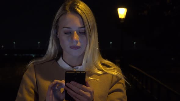 A Young Beautiful Woman Works on a Smartphone in an Urban Area at Night