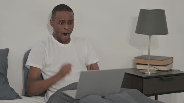 African Man Celebrating Success on Laptop in Bed