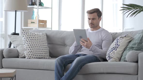 Serious Man Using Tablet While Sitting on Sofa