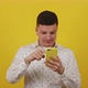Portrait of a Surprised Guy 20 Years Old Who Holds a Phone in His Hands on a Yellow Background - VideoHive Item for Sale