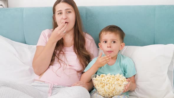 Portrait of Family in Pajamas Lying Bed with Big of Popcorn and Watching Movie on Weekend Morning