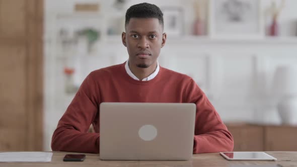 African Man Showing Thumbs Down Sign While using Laptop in Office