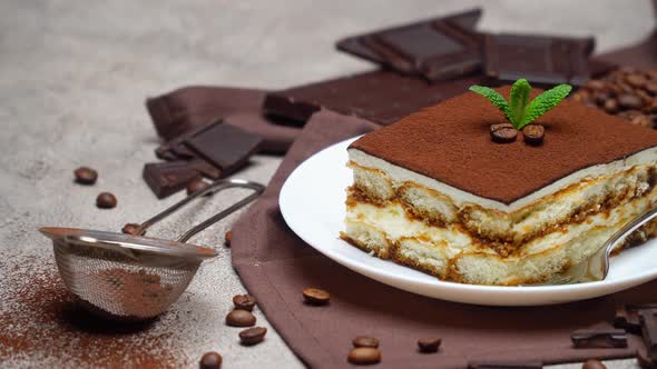 Portion of Traditional Italian Tiramisu dessert and coffee beans on grey concrete background