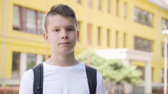 A Caucasian Teenage Boy Smiles at the Camera  Closeup  a School in the Background