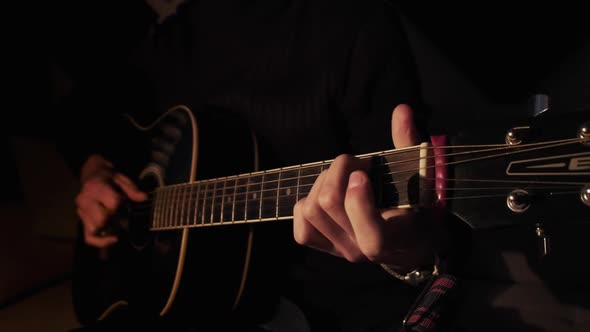 Man Playing Acoustic Guitar at Home in Atmospheric Dark Warm Lighting