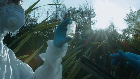 Chemists Wearing Ppe Suits Taking Sample of Swamp Water for Toxicity Testing Typing in Gadget Tablet