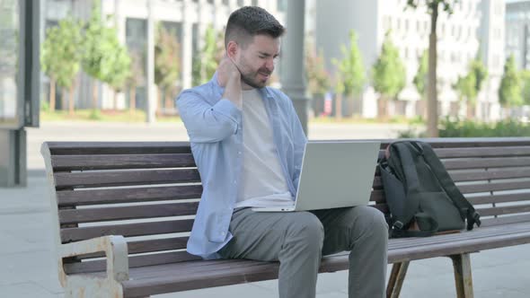 Young Man with Neck Pain Using Laptop While Sitting on Bench