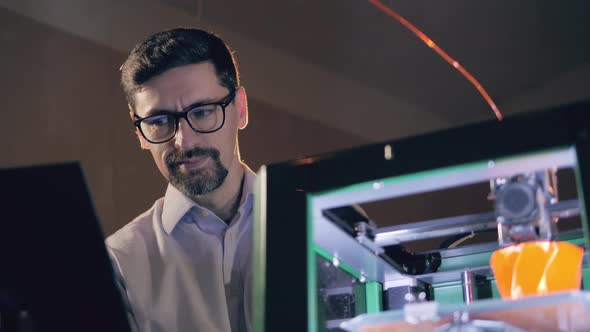 An Engineer with a Laptop Is Watching 3D-printer at Work