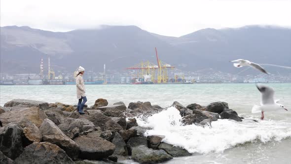 Woman is walking by empty seafront in windy weather with crashing sea waves