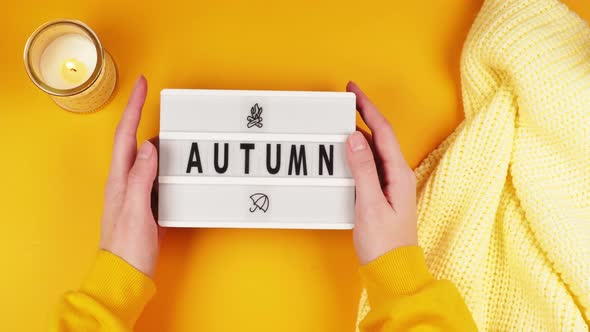 Hands of a young girl hold a white board with the inscription Autumn