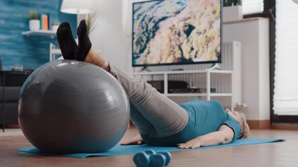 Old Woman Stretching Legs Muscles on Fitness Toning Ball