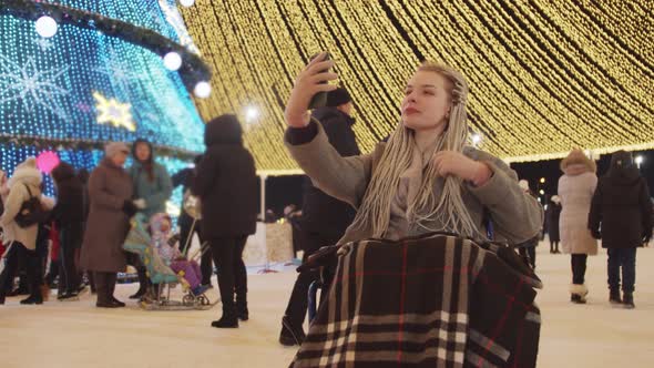 Young Woman in a Wheelchair at Christmas Celebrating on the Streets Taking a Photo and Fixes Her