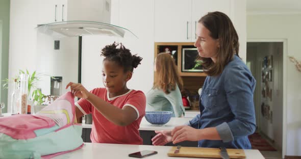 Happy caucasian woman and her african american daughter packing food together