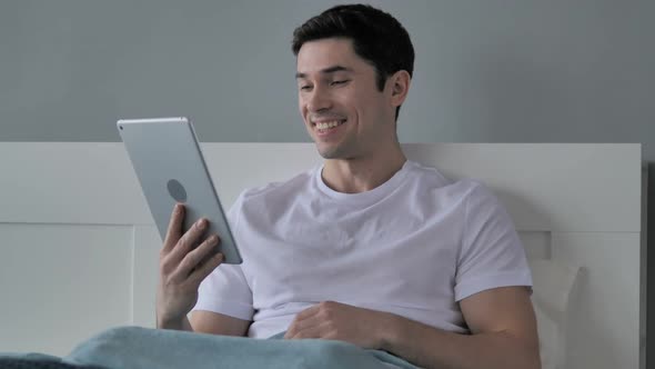 Online Video Chat on Tablet By Young Man in Bed