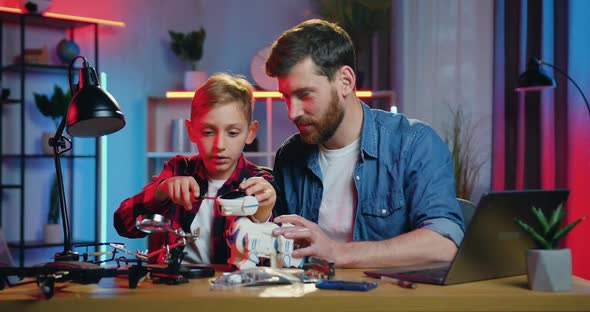 Father and His Curious Son Repairing Robot Using Screwdriwers Sitting at Workplace in the Evening