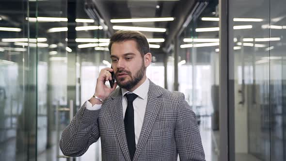 Modern Bearded Businessman Walking Through the Office Hall and Talking on Phone