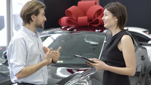Cheerful Wealthy Man Talking with Car Dealer in Showroom. Side View of Positive Caucasian Buyer and