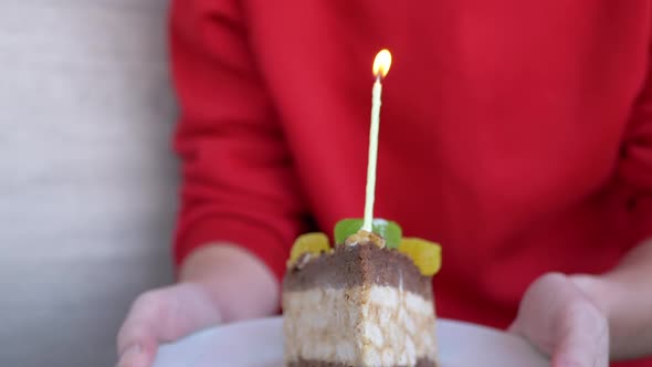 A Woman Holds a Plate with a Piece of Birthday Cake and One Lighted Candle