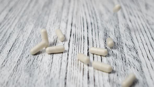 White medical capsules are thrown on a wooden vintage table