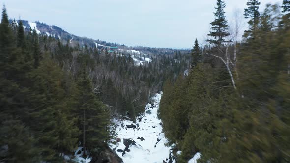 Aerial flyover person walking on bridge over frozen river in winter snow pine tree forest in nationa