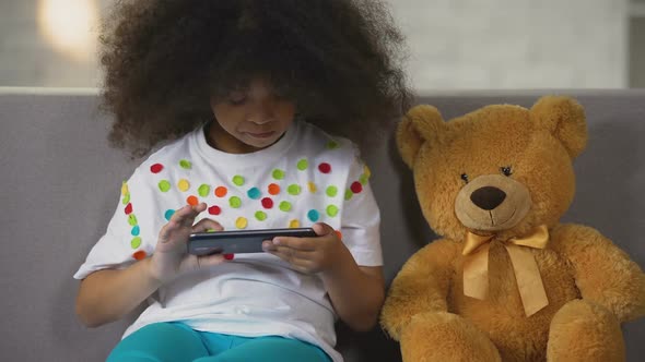 Funny Black-Haired Girl Sitting on Sofa and Playing Game on Smartphone, Rest