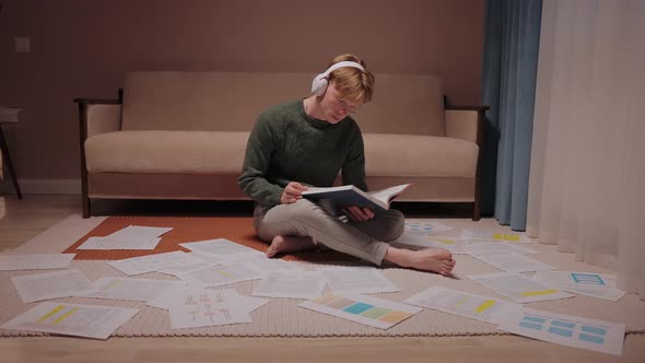 Guy Sits on the Floor Surrounded By Papers and Notes Listens Music at Home