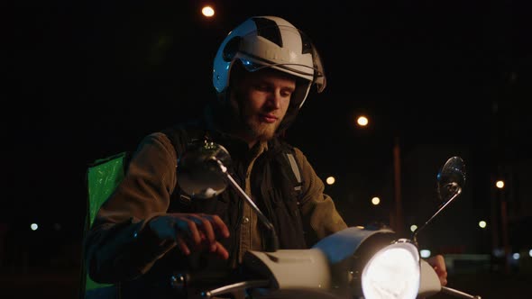 A Male Courier Starts a Scooter to Deliver Dinner to Customers