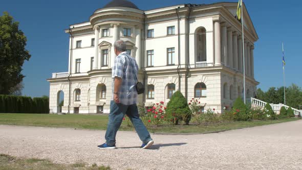 Grey Haired Old Man Walks Along Green Park Zone Against Sky