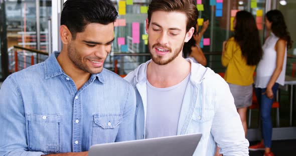 Male executives shaking hands while using laptop