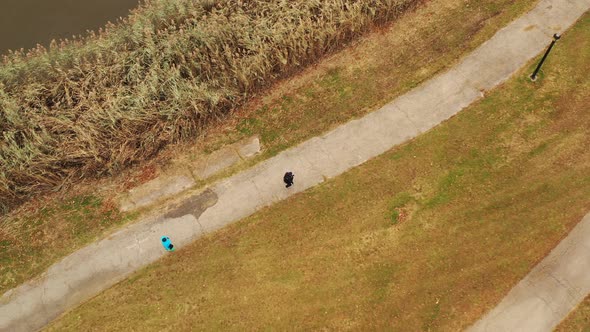 a bird's eye view over two strangers walking in the same direction, along a paved walkway. It is a c