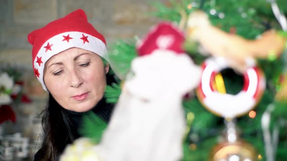 Woman Prepares Christmas Tree at Home Wearing a Christmas Red Hat