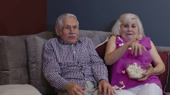 Scared Senior Old Couple Holding Popcorn Watching Horror Tv Show Film Sitting on Sofa in Living Room