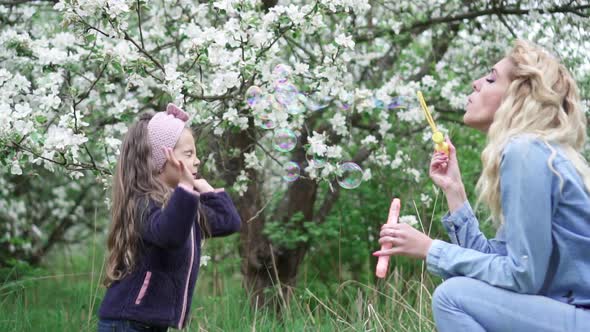 Mom and Little Daughter Playing with Soap Bubbles in Blooming Garden, Slow Motion