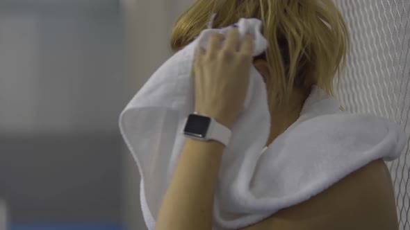 Close-up Side View of Young Perspiring Sportswoman Wiping Face with White Towel. Exhausted Young