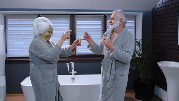 Elderly Grandmother with Facial Green Mask and Grandfather with Shaving Foam Dancing in Bathroom