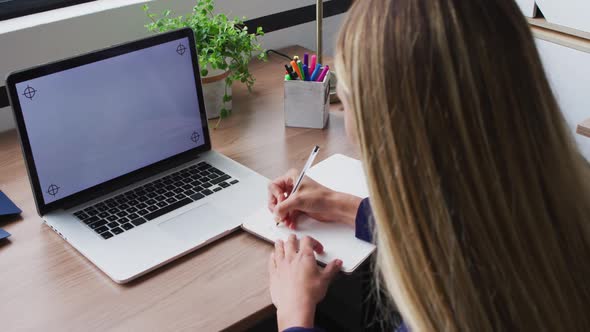 Caucasian businesswoman taking notes during video call, using laptop with copy space on screen