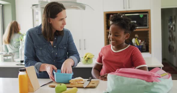 Happy caucasian woman and her african american daughter packing food together