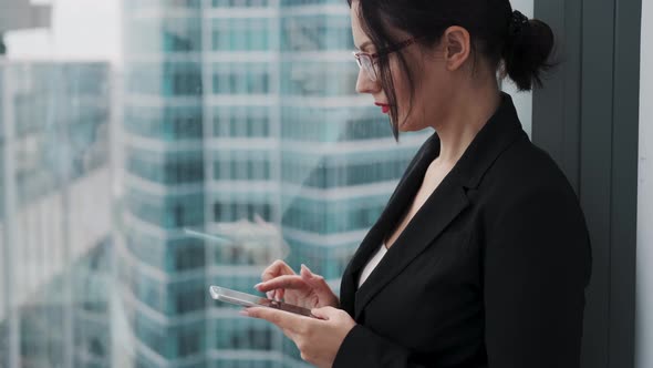 Businesswoman Using a Cell Phone While Standing on a High Floor of a Skyscraper Near a Window.