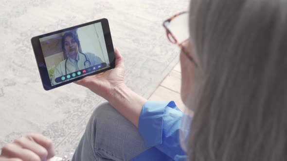 Over Shoulder View of Old Woman Video Calling Virtual Doctor on Tablet at Home