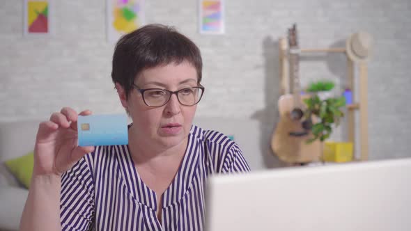 Frustrated Woman Sitting at a Laptop with a Bank Card in Hand