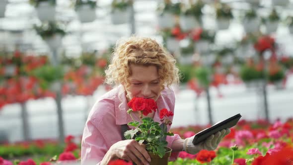 Curly Blonde with a Digital Tablet Enjoys the Smell of Flowers