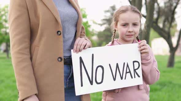 A girl with her mother is holding a banner with the inscription text "No to war".