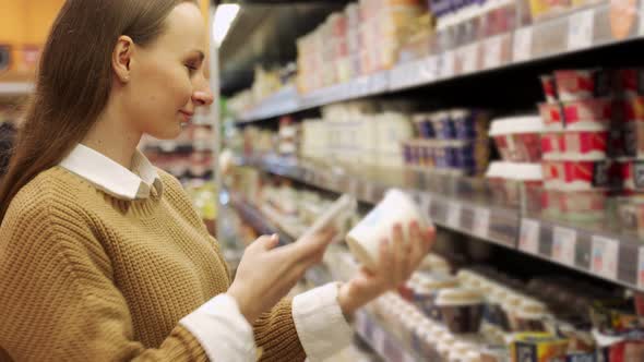 A Young Woman Takes Products From a Supermarket Shelf Holds a Smartphone Scans the Barcode on the