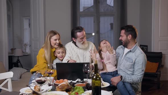 Family Idyll During Review the Amusing Photos on Computer at the Festive Dinner Table