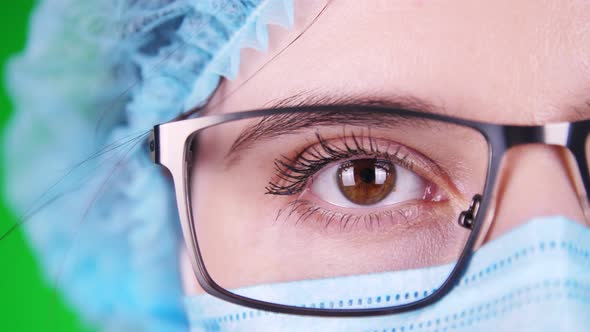 Green Background. Close-up, Eye, Part of Female Doctor Face in Glasses, in Blue Medical Mask and