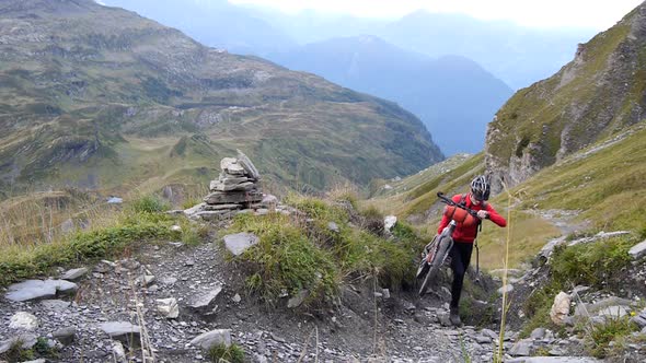 A man walking with his mountain bike on a trail in a European mountain range