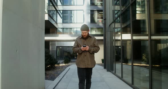 A Young Man is Typing on a Mobile Phone While Walking Around the Business Center